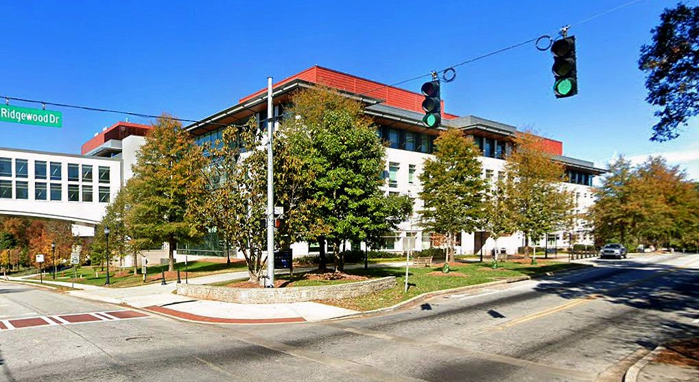 A red-roofed building surrounded by trees at a street corner with a traffic light.